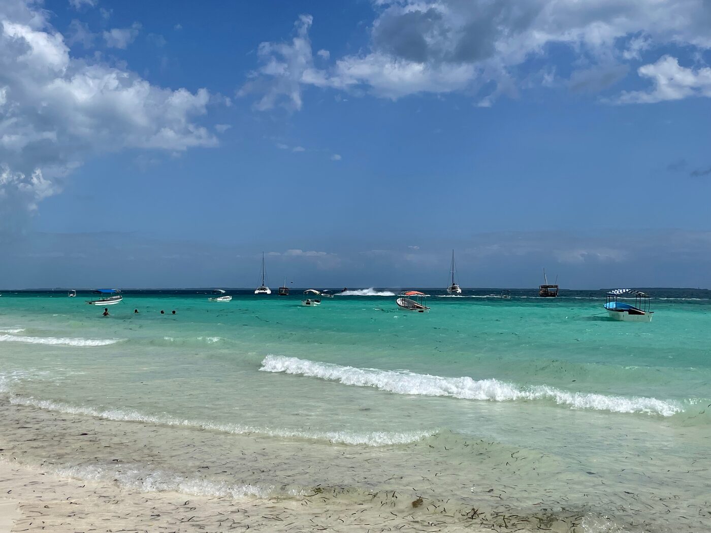 Boats anchored off a calm white-sand beach
